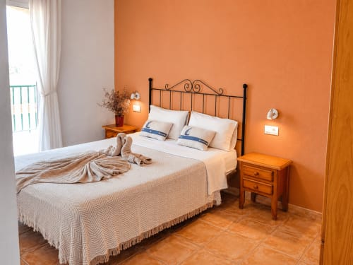 Bedroom with orange walls, black wrought iron bed, wooden nightstand, and sea view balcony at Apartamentos El Calón Playa,