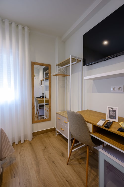 Habitación moderna del Hotel Alcazaba Salobreña con escritorio de madera, silla, cama litera, espejo y cortinas blancas