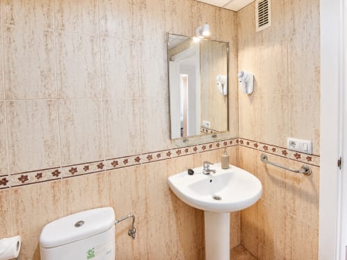 Modern bathroom with beige tile walls, pedestal sink, mirror, and grab bars at Apartamentos El Calón Playa, Cuevas del