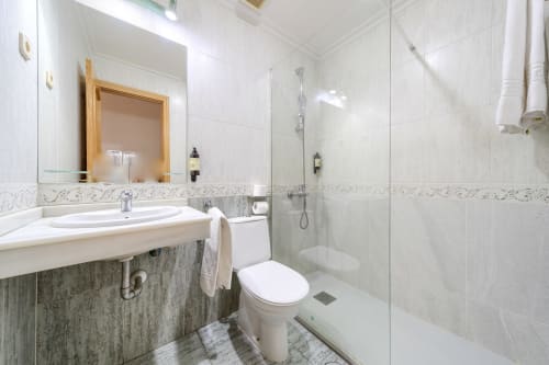 Baño moderno del Hostal El Molino con azulejos blancos, lavabo, inodoro y cabina de ducha de vidrio en Collado Villalba
