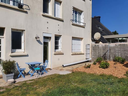 Beachside apartment patio in La Fôret-Fouesnant with lawn, blue chairs, and coastal stone wall.