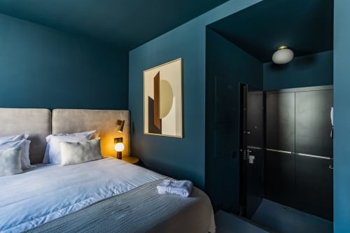 Quarto de estúdio compacto moderno com paredes azul-petróleo, cama com cabeceira cinza, iluminação amarela e guarda-roupa preto no Porto