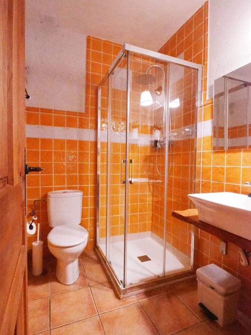 Baño moderno con paredes de azulejos naranjas, ducha de cristal, inodoro y lavabo blancos en Apartamentos Senda del Duratón