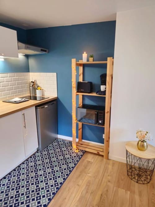 Kitchenette moderne dans l'appartement Sous les Toits à Gîtes Saint Valéry en Caux avec mur d'accent bleu et étagères en bois