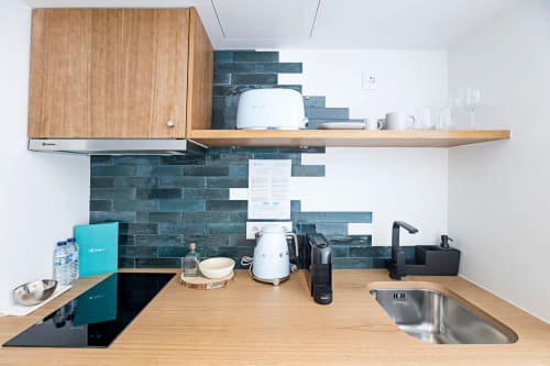 Kitchenette moderna em quarto de hotel no Porto com armários em madeira, azulejos teal na parede e eletrodomésticos