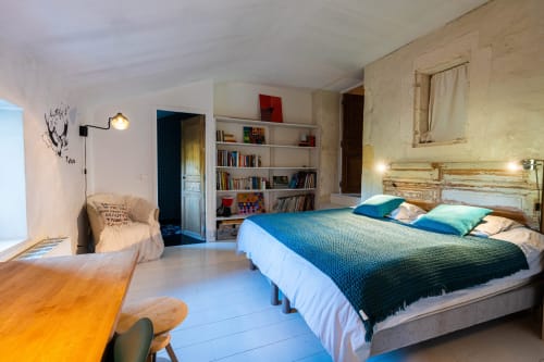 Chambre du Mas F à Saint-Rémy-de-Provence avec literie bleue, tête de lit en bois, bibliothèque et vue sur le jardin