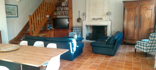 Spacious living room at Logis de Chenac cottage with blue sofa, fireplace, wooden staircase and dining area