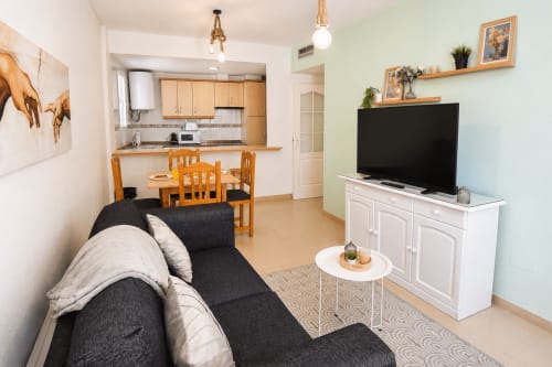 Sala de estar moderna con sofá negro, TV, comedor y cocina abierta en Apartamentos El Calón Playa, Cuevas del