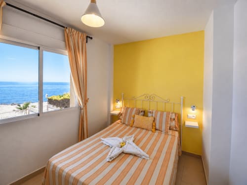 Dormitorio luminoso con vista al mar, pared amarilla, cama con sábanas rayadas en Apartamentos El Calón Playa, Cuevas