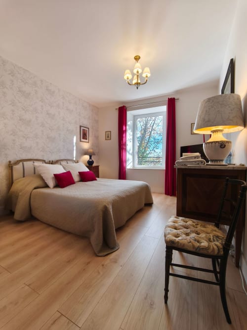 Chambre Perle avec literie beige, coussins rouges, parquets, lustre en laiton à la Magnanerie de Sainte Croix