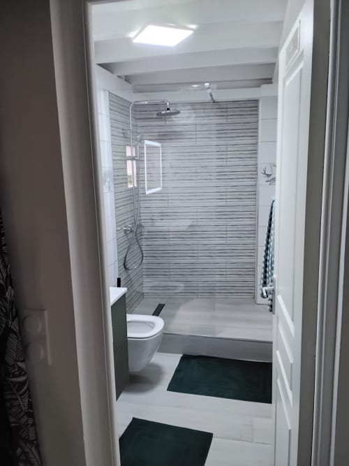Salle de bain moderne avec douche à l'italienne, carrelage rayé, sanitaires blancs et accents de sol sombre à l'appartement Kay Betty,