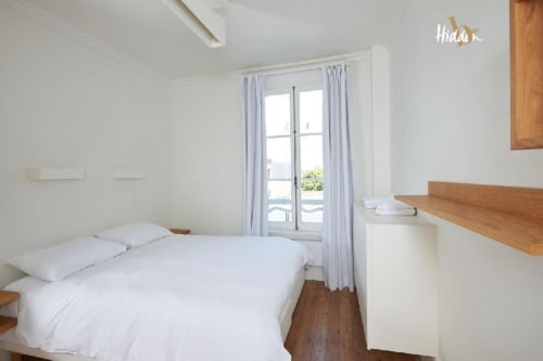 Bright suite bedroom at Hidden Bay Hotel with white bedding, wooden desk, balcony doors overlooking Cayeux-sur-Mer city view