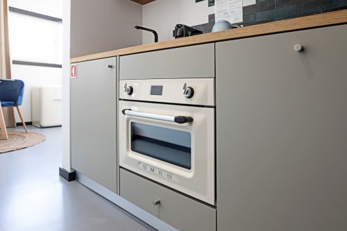 Kitchenete moderna no estúdio do hotel Benefit Collection no Porto, com fogão creme, cooktop e acabamentos em madeira