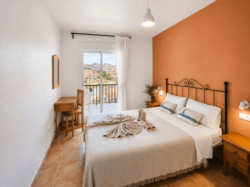 Bright bedroom with orange accent wall, double bed, wooden furniture, and sea view balcony at Apartamentos El Calón Playa