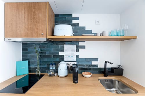 Kitchenete moderna em estúdio de hotel no Porto com azulejos azul-turquesa, bancadas de madeira, pia em aço inoxidável e eletrodomésticos compactos