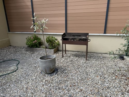 Garden patio at Les Gites De Flaubert villa with gravel, potted plants, grill, and wooden fence backdrop