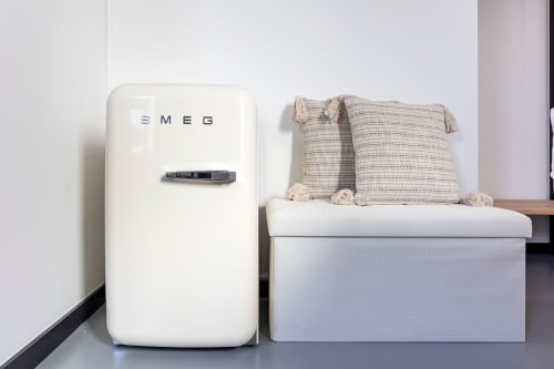 Geladeira SMEG retrô ao lado de banco de armazenamento branco com almofadas com listras bege em apartamento-estúdio de hotel no Porto