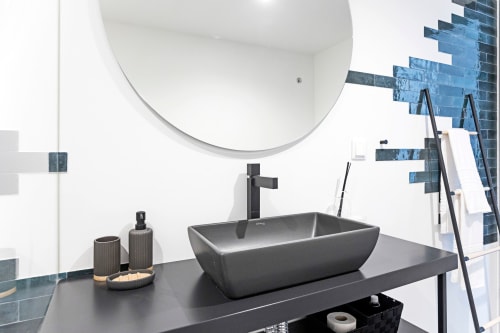 Modern bathroom in Porto hotel studio with dark vessel sink, black faucet, round mirror, and blue tile accents