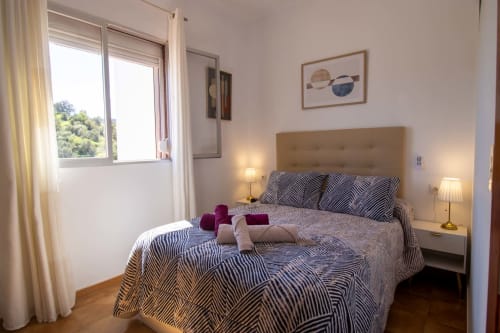 Dormitorio luminoso en la casita La Casa de Tita Clota, Setenil de las Bodegas, con ropa de cama a rayas, cabecero beige y balcón