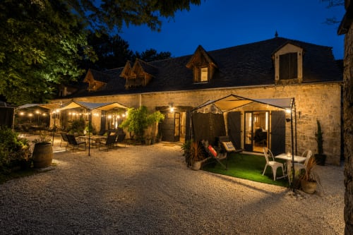 Cour du Domaine Valenquercy la nuit : bâtiment en pierre, espaces de détente illuminés et terrasses à Le