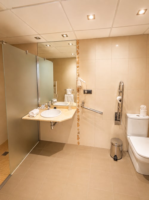 Baño moderno y accesible en Hotel Villa de Cacabelos con ducha a ras de suelo, doble lavamanos y barras de apoyo