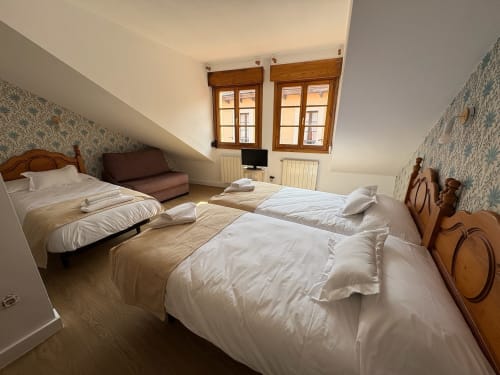 Habitación triple de Pensión Argüelles en Ribadesella con tres camas, muebles de madera y vistas a la ciudad