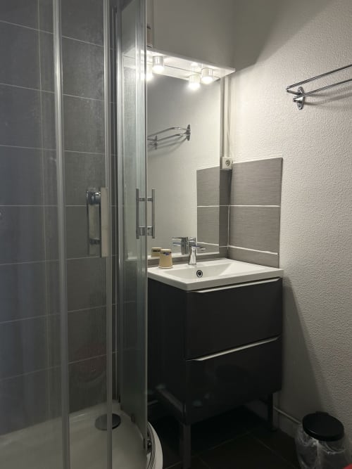 Salle de bain moderne de l'hôtel BDM Montastruc-la-Conseillère avec meuble vasque noir, lavabo blanc, miroir et douche vitrée
