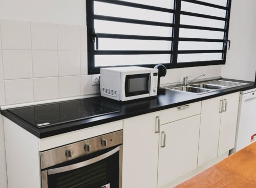 Cuisine moderne de l'appartement Cocon de Kess à Cayenne, avec plan de travail noir, armoires blanches, micro-ondes et inox