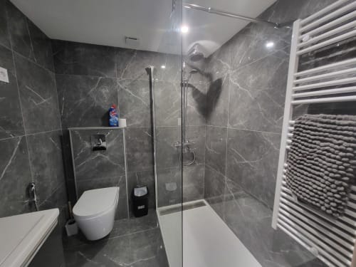 Salle de bain moderne avec carrelage en marbre noir, douche à l'italienne, toilettes blanches et sèche-serviettes chauffant aux Gîtes Les Camélias 71