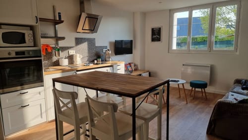 Modern kitchen-dining area with wooden table, white chairs, and river view at Ô Loch apartment in La Fôret-Fouesnant