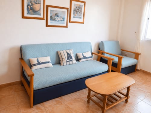 Living room with blue sofa bed, wooden armchair, and coffee table in Apartamentos El Calón Playa, Cuevas del Almanzora