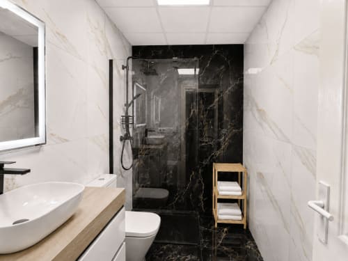 Baño moderno con cabina de ducha en mármol negro, lavabo blanco, inodoro y estantería de madera en Apartamentos El Calón