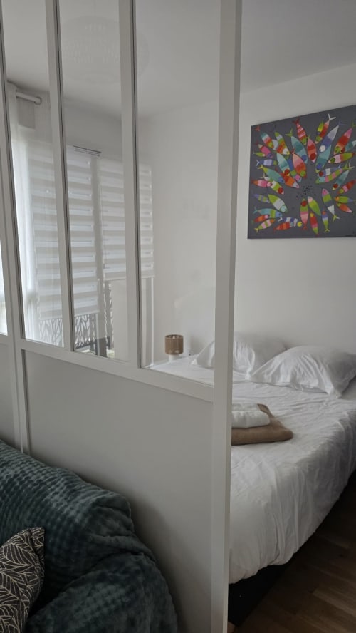 Modern bedroom with white framed glass partition, white bedding, colorful abstract bird artwork, and open balcony access at Ô
