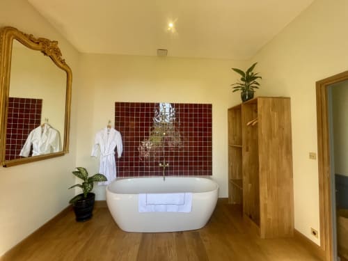 Luxueuse salle de bain spa au Château de Vaux Morvan avec baignoire blanche indépendante, carrelage bourgogne, parquet et vue sur le jardin
