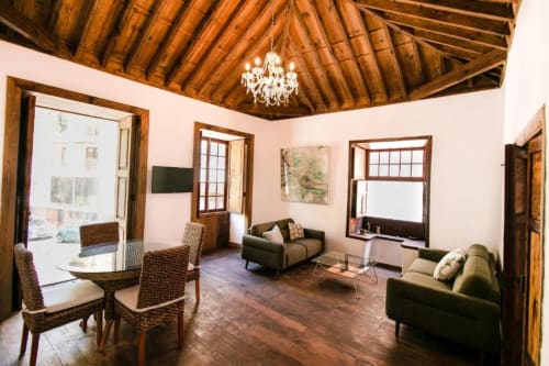 Sala de Casa 1820 con vigas de madera, araña, comedor, sofás y vistas al jardín en Santa Cruz de la Palma