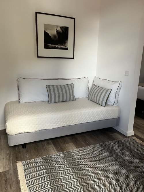 Sofá-cama moderno no quarto Rum Inn II, Calheta Madeira, com almofadas listradas e tapete geométrico