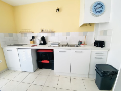 Cuisine moderne de l'appartement Ibis Rouge à l'hôtel Maisons En Or, Sinnamary, avec armoires blanches, cuisinière, évier et touches de jaune