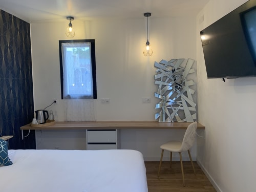 Modern hotel room at La Maison Blanche with work desk, flat-screen TV, geometric wall art, and pendant lighting