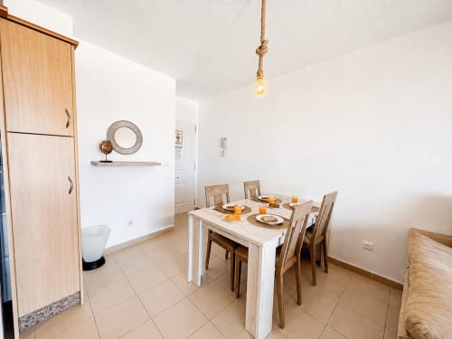 Comedor luminoso con mesa de madera, sillas y lámpara colgante de cuerda en Apartamentos El Calón Playa, Cuevas del Almanzora