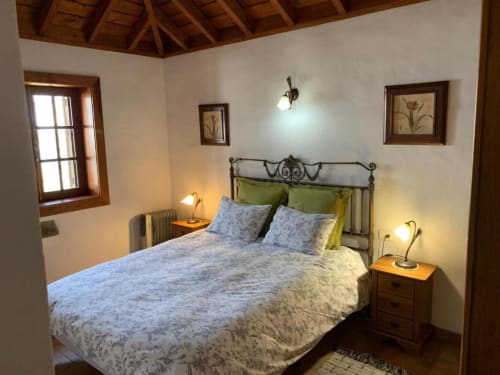 Acogedora habitación en Villa El Topo con cama de hierro forjado, cojines verdes, vigas de madera y mesas de noche de terracota en la zona rural