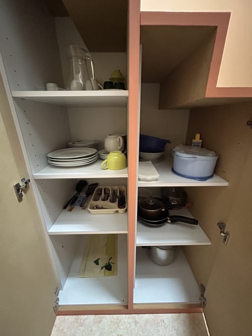 Placard de cuisine ouvert dans l'appartement de Luxeuil-les-Bains présentant vaisselle, batterie de cuisine, ustensiles et couverts organisés sur blanc