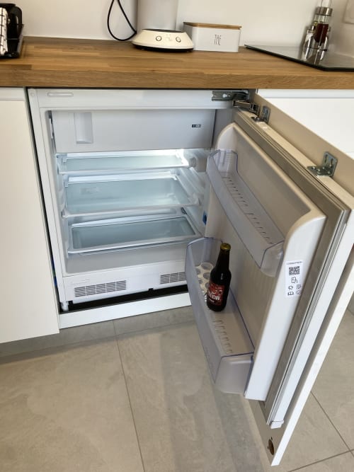 Réfrigérateur blanc ouvert dans la cuisine de l'Appartement 7 à La Maison Blanche, Bouguenais, avec une bouteille de bière visible sur l'étagère