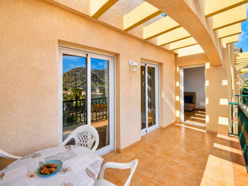 Sunny terrace at Apartamentos El Calón Playa with dining table, sea views, and hillside landscape
