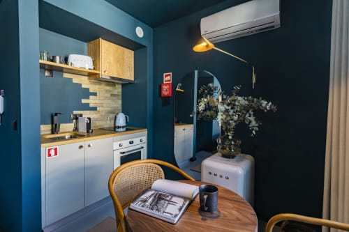 Pequena cozinha moderna com paredes azul-esverdeadas, mesa de jantar em madeira e eletrodomésticos brancos em hotel no Porto
