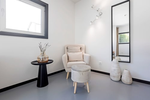 Área de estar moderna em estúdio de hotel no Porto com poltrona creme, puff, espelho e decoração minimalista