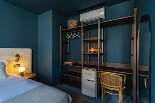Moderno estúdio no Porto com paredes azul-petróleo, guarda-roupa em madeira, área de trabalho, frigorífico vintage branco e cama com acentos amarelos.