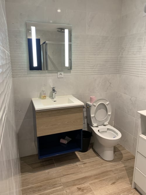Salle de bains moderne du Restaurant du Port avec vasque blanche, toilettes, miroir éclairé et sol aspect bois