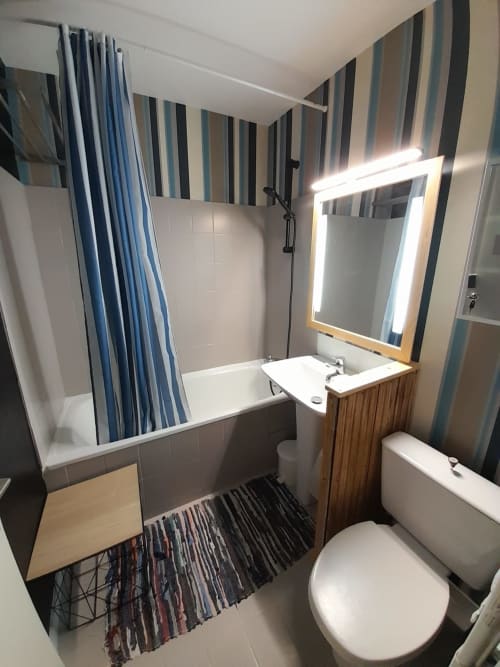 Salle de bain moderne chez Mer et Maisons avec baignoire, lavabo, toilettes, papier peint à rayures et miroir illuminé