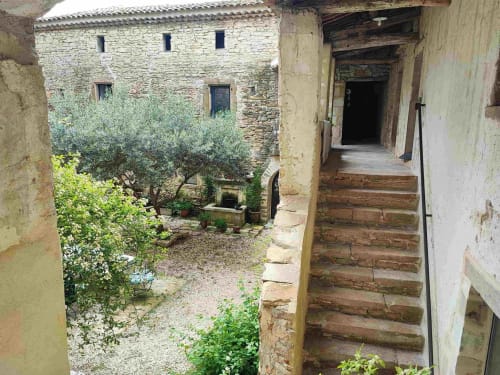 Cour rustique en pierre avec olivier à la Magnanerie de Sainte Croix, escalier en bois menant à l'entrée d'un appartement