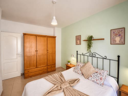 Dormitorio luminoso en Apartamentos El Calón Playa con cama de hierro forjado, armario de madera y paredes verde menta